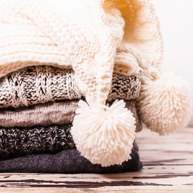Ein Stapel gestrickter Schals und eine Mütze mit Bommeln.