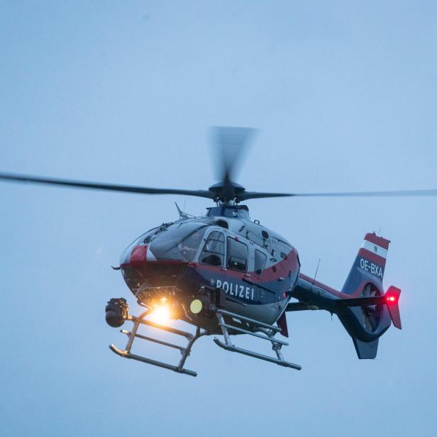 Ein rot-blau-weisser Polizei-Hubschrauber mit der Kennung OE-BXA ist in der Luft.
