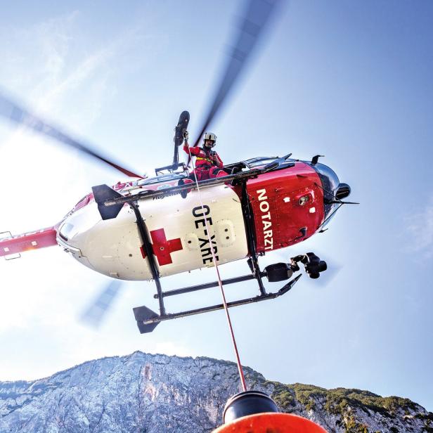 Ein rot-weißer Notarzthubschrauber der Flugrettung im Einsatz vor einer Bergkulisse.