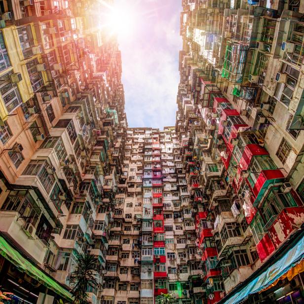 Blick nach oben zwischen dicht gedrängten Wohnhäusern in einer asiatischen Stadt.