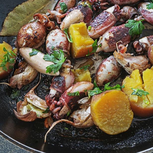 Gebratene Calamaretti mit Kürbis, Knoblauch und Kräutern in einer schwarzen Pfanne.
