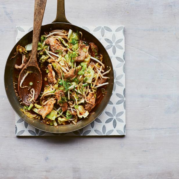 Eine Pfanne mit gebratenem Schweinefleisch, Kohl und Sojasprossen auf einem Küchentuch.