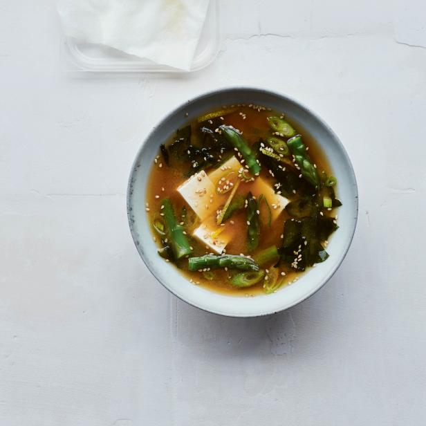Eine Schüssel Misosuppe mit Tofu, Algen und Frühlingszwiebeln, daneben ein Block Tofu.