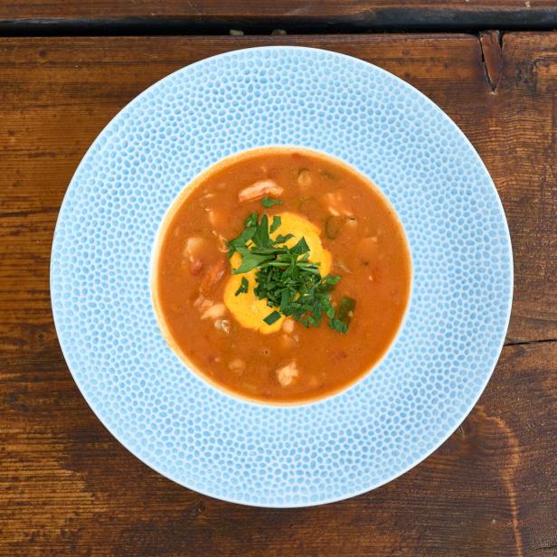 Eine Schüssel mit Tomatensuppe, garniert mit einem Klecks Creme und Petersilie, auf einem blauen Teller.