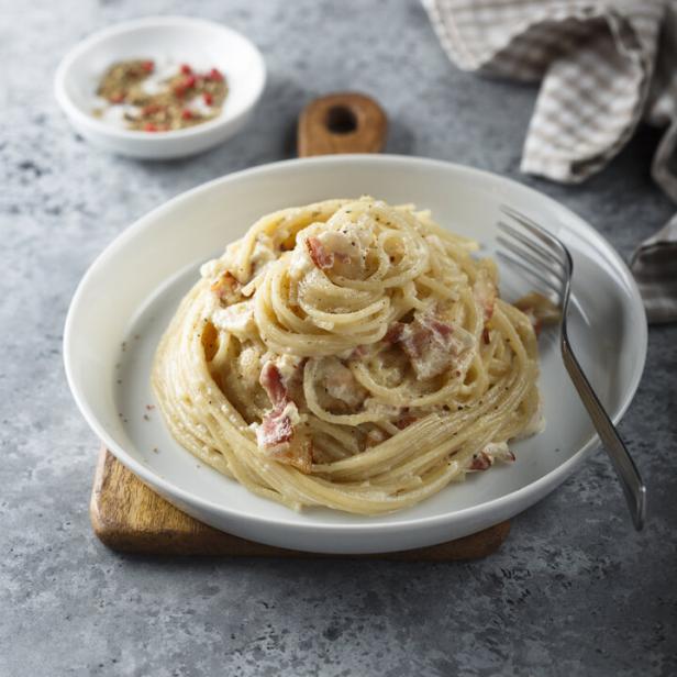 Ein Teller Spaghetti Carbonara steht auf einem Holzteller.