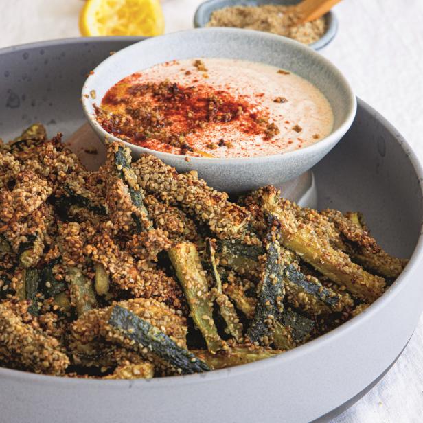 Ein Teller mit frittierten Zucchinischeiben und einem Dip mit Gewürzen garniert.