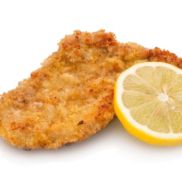 Ein paniertes Schnitzel liegt neben einer halbierten Zitronenscheibe auf weißem Hintergrund.