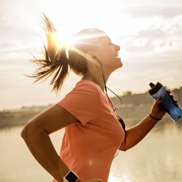 Eine Frau läuft in der Morgensonne mit einer Trinkflasche in der Hand.