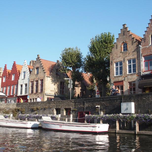 Blick auf einen Kanal in Brügge mit Booten und historischen Gebäuden am Ufer.