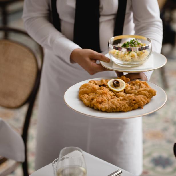 Ein Kellner serviert ein Wiener Schnitzel mit Kartoffelsalat.
