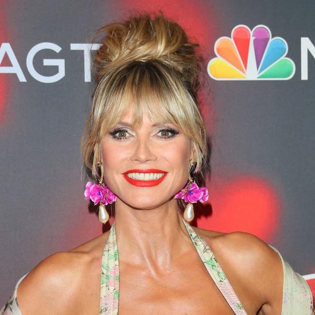 Heidi Klum lächelt vor einem Hintergrund mit dem Logo von „America's Got Talent“.