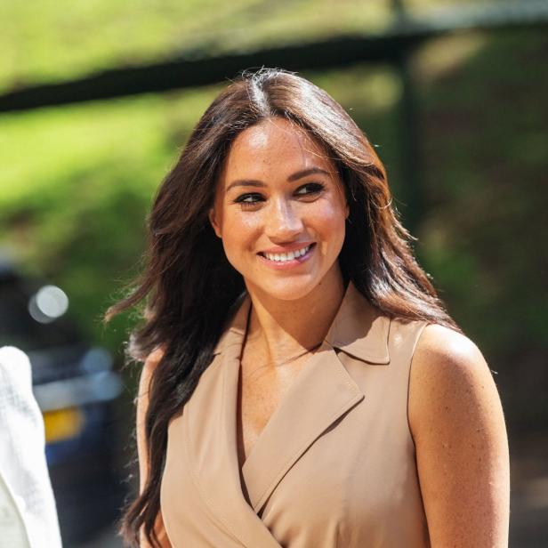 Meghan Markle lächelt in einem beigefarbenen Kleid.