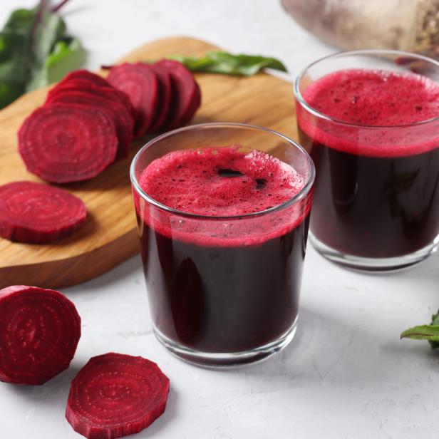 Zwei Gläser Rote-Bete-Saft stehen neben geschnittenen Rüben auf einem Tisch.