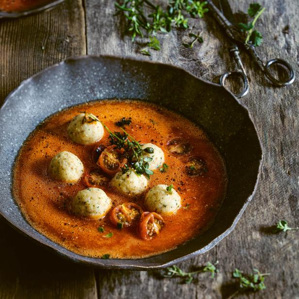Eine Schüssel mit Tomatensuppe und Kräutern, garniert mit Knödeln und Tomatenstücken.