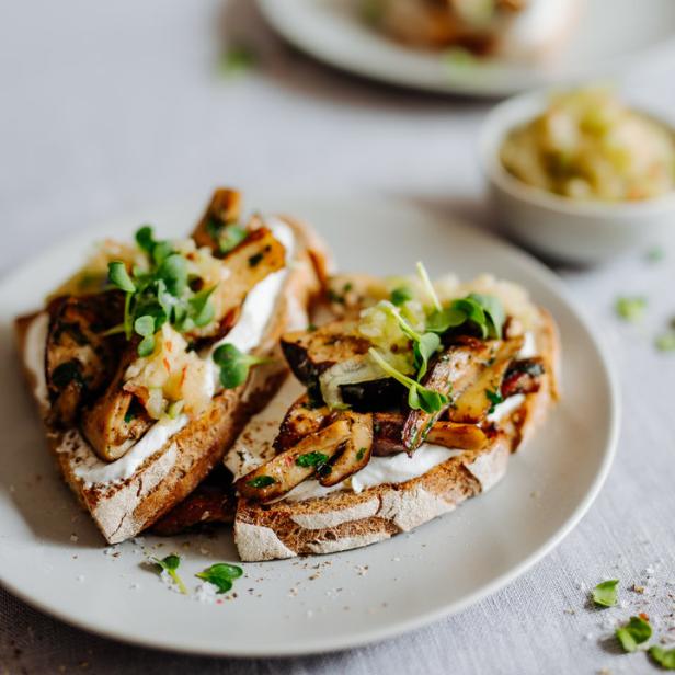 Zwei Toasts mit Pilzen, Frischkäse und Sprossen auf einem Teller.