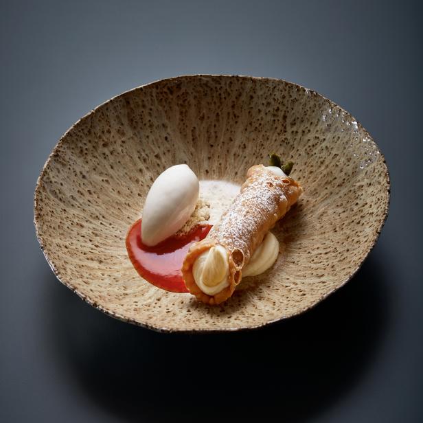 Ein Ricotta-Cannolo mit Puderzucker, Eis und roter Sauce auf einem Teller.