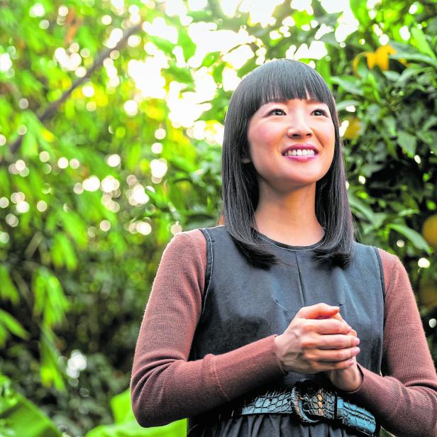 Marie Kondo lächelt vor einem Baum mit Früchten.