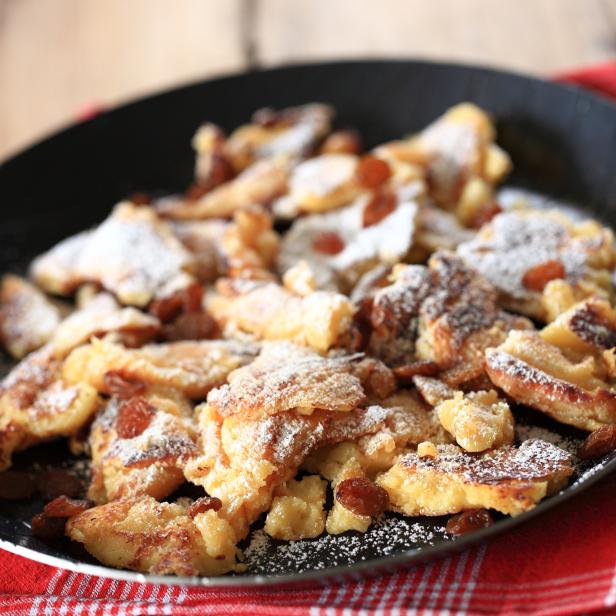 Kaiserschmarrn mit Rosinen und Puderzucker in einer Bratpfanne.