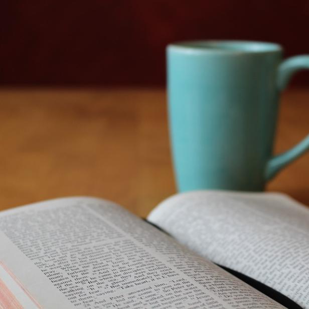 Eine geöffnete Bibel liegt neben einer hellblauen Tasse.