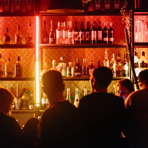 In einer Bar stehen mehrere Personen vor einem Regal mit Spirituosenflaschen.