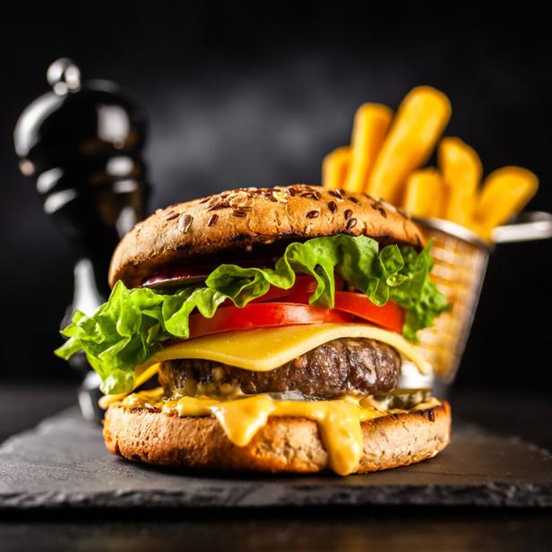 Ein Burger mit Salat, Tomaten und Käse, serviert mit Pommes Frites.