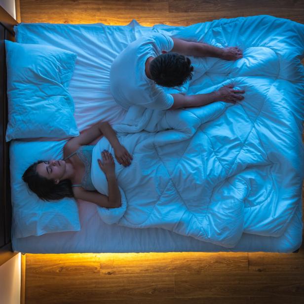 Ein Mann sitzt im Bett, während eine Frau neben ihm schläft.