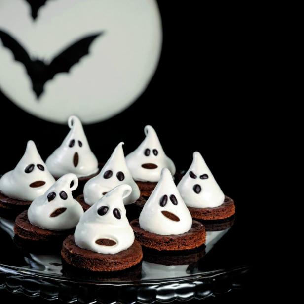 Geisterförmige Süßigkeiten stehen vor einem Mond mit einer Fledermaus für Halloween.