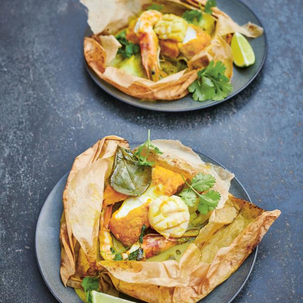 Zwei Teller mit Fisch und Meeresfrüchten in Pergamentpapier serviert.
