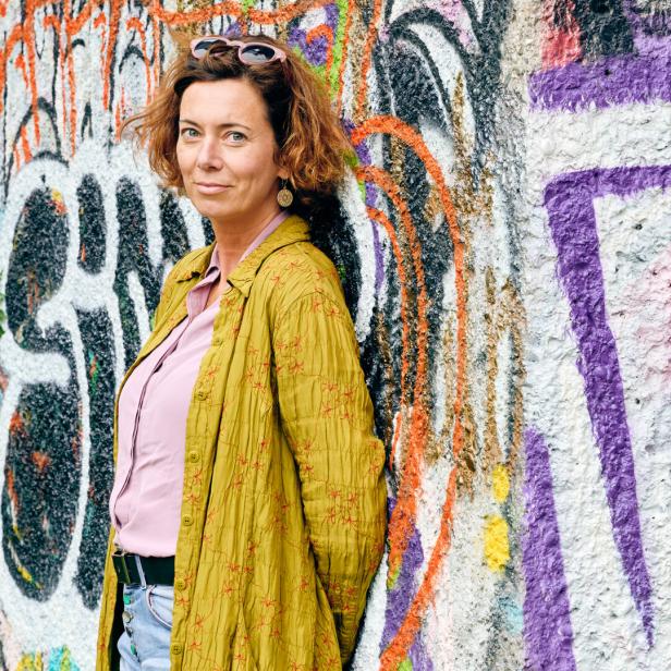 Eva Menasse steht vor einer mit Graffiti bemalten Wand.