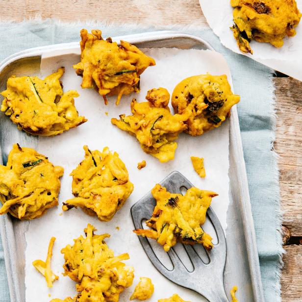 Frittierte Gemüsebällchen, sogenannte Pakoras, auf einem Backblech mit Backpapier.