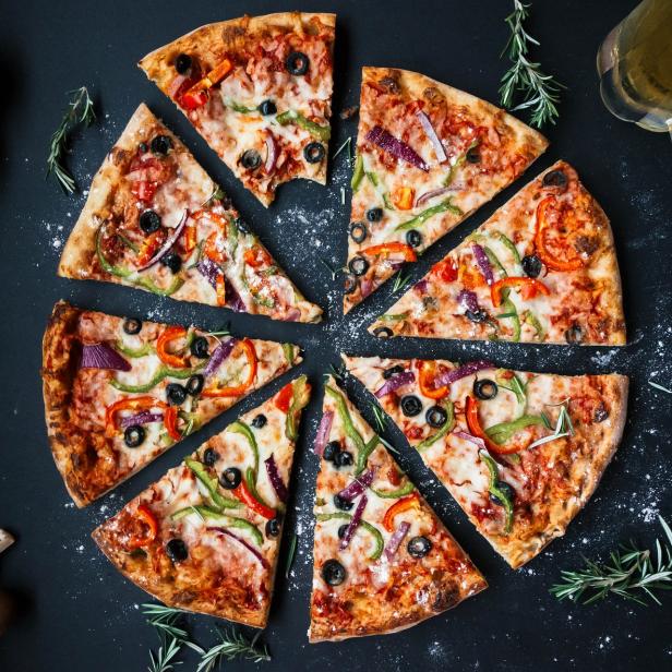 Eine Pizza mit Paprika, Oliven und Zwiebeln, von der ein Stück fehlt, neben einem Bierglas.