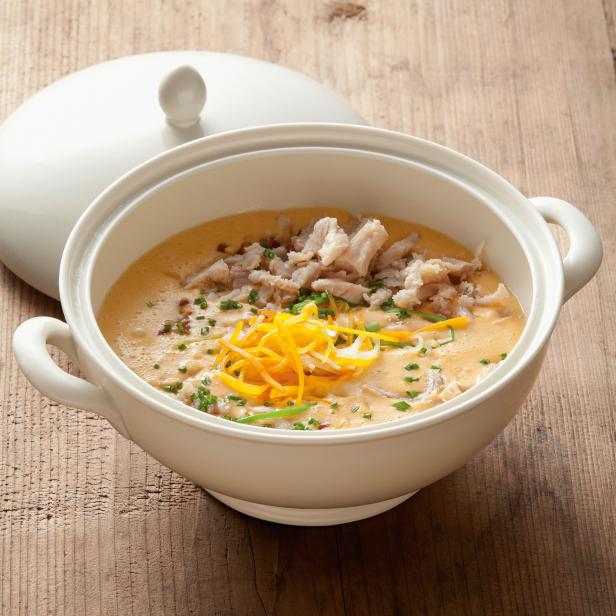 Eine cremige Suppe mit Fischstücken und Karottenstreifen in einer weißen Schüssel.