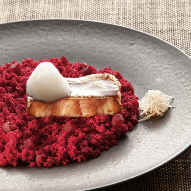 Ein Teller mit einem Stück Fisch auf rotem Couscous und einer weißen Schaumkrone.