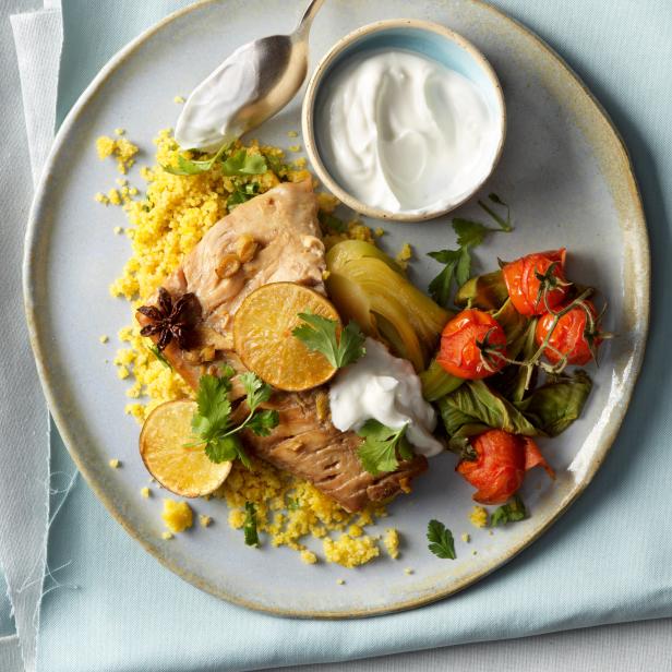 Ein Teller mit Hähnchen, Couscous, Joghurt und gebratenen Tomaten wird von oben gezeigt.