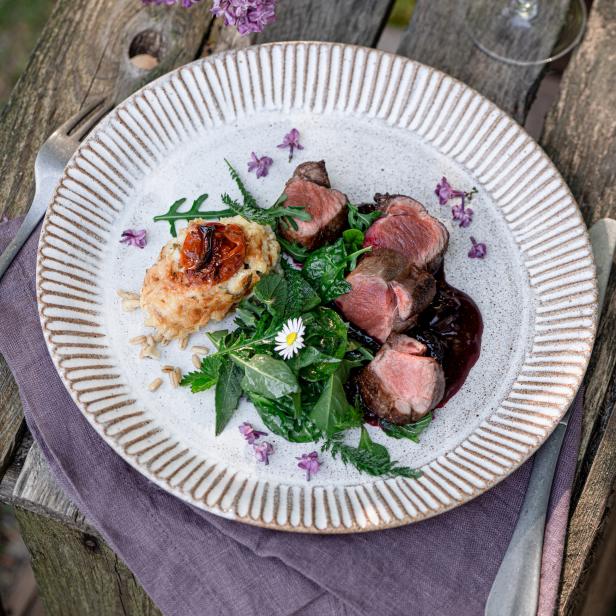 Ein Teller mit medium gebratenem Fleisch, Kartoffeln und Salat auf einem Holztisch angerichtet.
