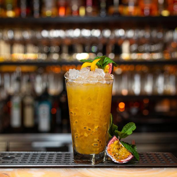 Ein mit Eiswürfeln gefülltes Glas mit einem gelben Cocktail, garniert mit Passionsfrucht und Minze.