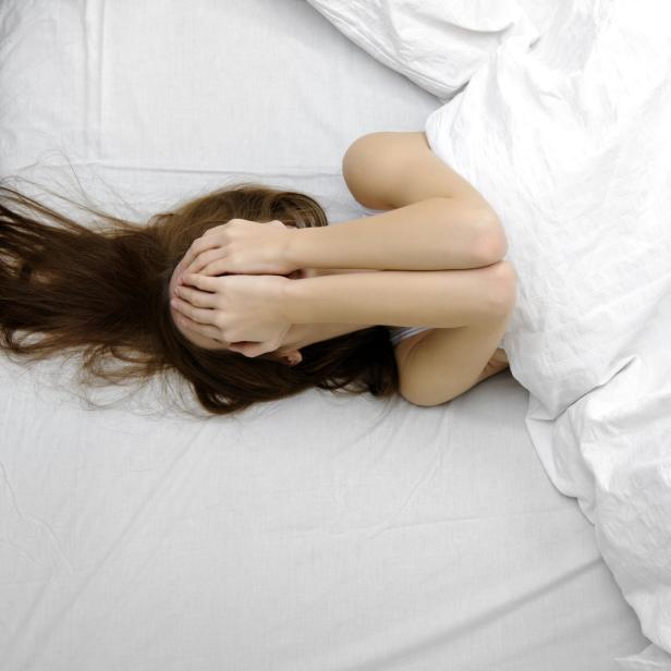 Eine Frau liegt im Bett und hält sich die Hände vors Gesicht.