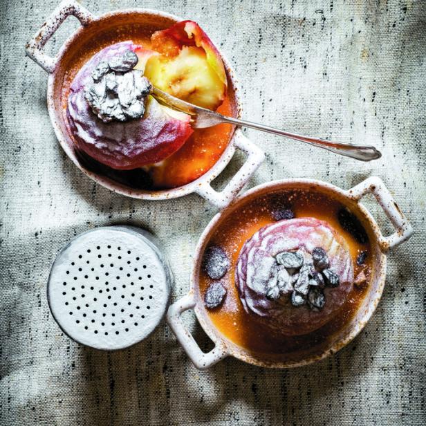 Zwei gebackene Äpfel mit Puderzucker und Trockenfrüchten in kleinen Schalen.