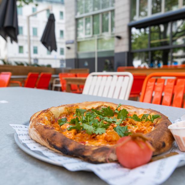 Eine Pizza mit Tomatensoße, Koriander und einem Klecks Soße auf einem Tisch im Freien.