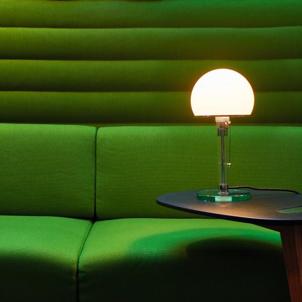 Eine beleuchtete Lampe steht auf einem kleinen Tisch vor einer grünen Wand.