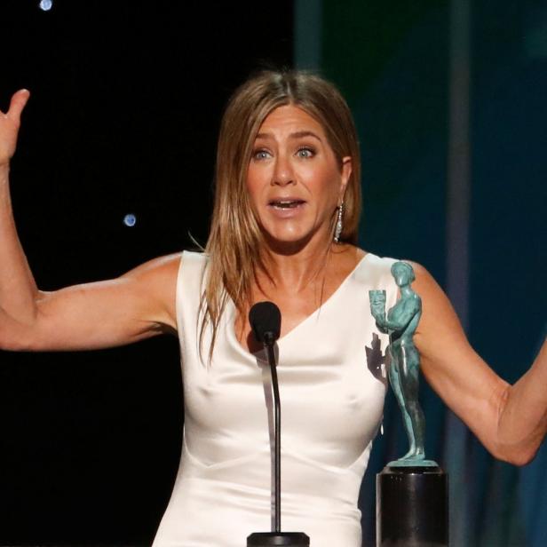 Jennifer Aniston hält eine Dankesrede mit einer Statue im Vordergrund.