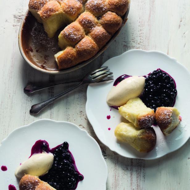 Zupfbrot mit Puderzucker, Blaubeeren und Eis auf Tellern angerichtet.