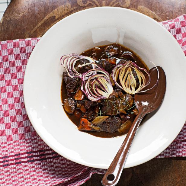 Ein Teller mit Boeuf Bourguignon, garniert mit Zwiebelringen, steht auf einem Küchentuch.