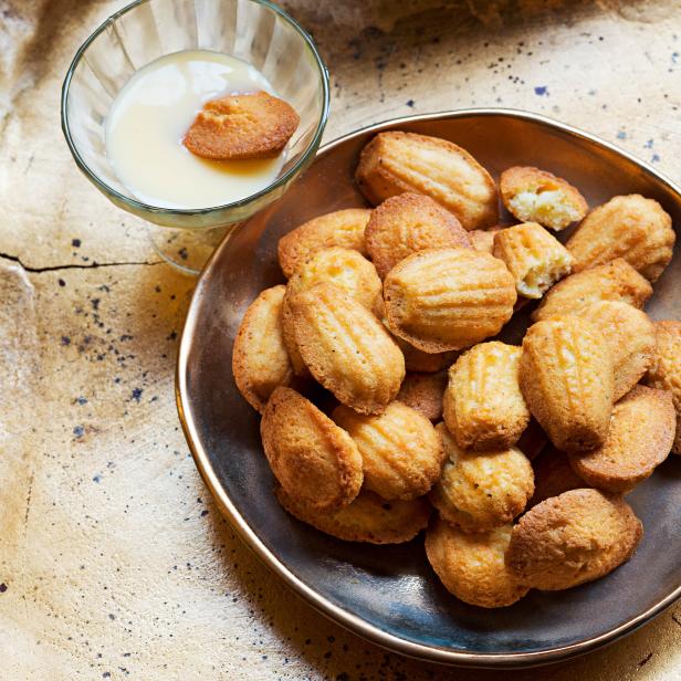 Eine Schale voller Madeleines und ein Glas mit Vanillesauce.