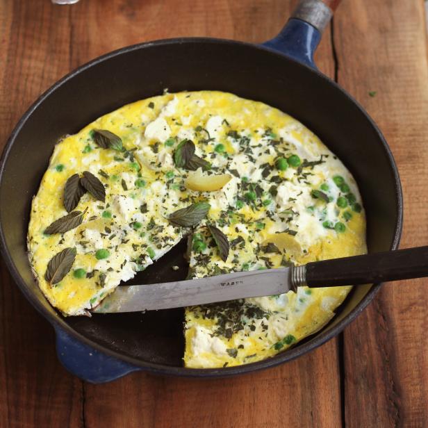 Eine Kräuter-Frittata mit Erbsen in einer Bratpfanne mit einem Messer darin.