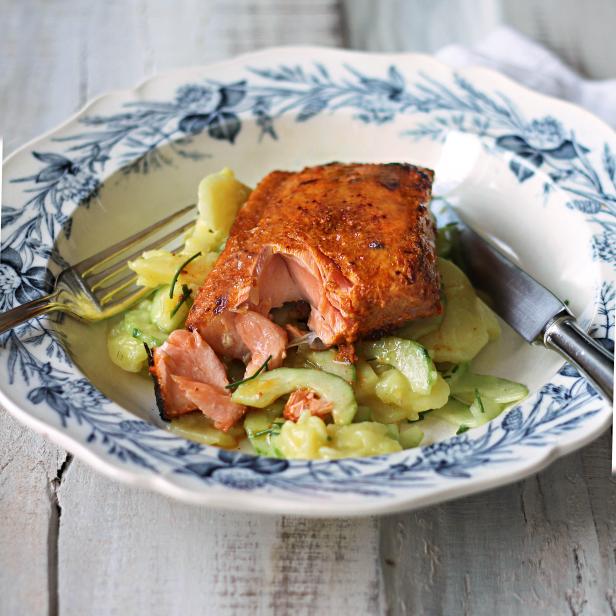 Ein Stück gebratener Lachs auf einem Teller mit Gurken- und Kartoffelsalat.