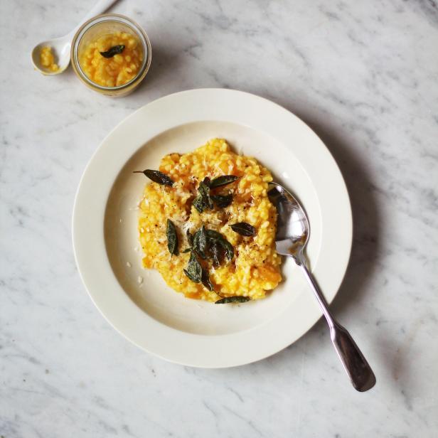 Ein Teller Kürbisrisotto mit Salbei und Parmesan auf einem Marmortisch.