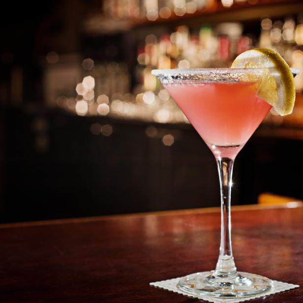 Ein rosa Cocktail mit Zuckerrand und Zitronenscheibe auf einer Bar.