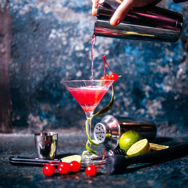 Ein Cocktail wird in ein Martiniglas gegossen, garniert mit Kirschen und Limettenzesten.