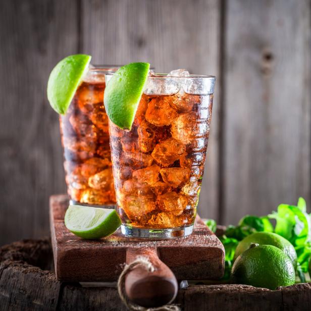 Zwei Longdrinks mit Limetten und Eiswürfeln auf einem Holzfass.